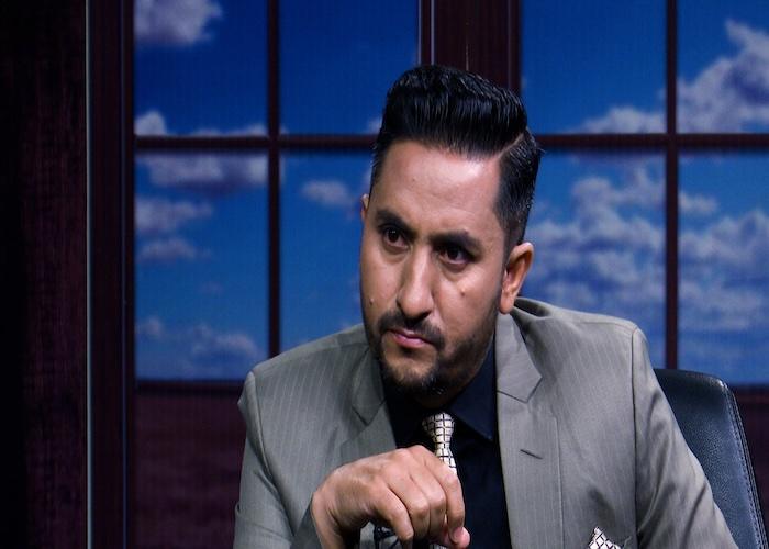 Jagadish Kharel seated in a suit with a serious expression during an interview setting.