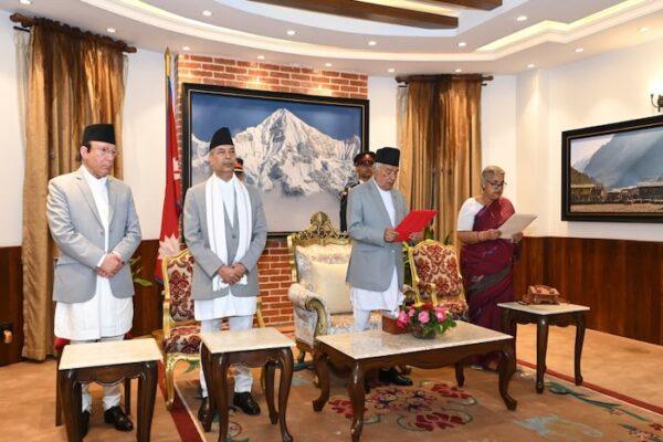 Group of Nepalese political leaders in formal attire standing in a room with a mountain painting in the background.