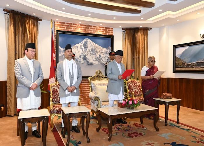 Group of Nepalese political leaders in formal attire standing in a room with a mountain painting in the background.