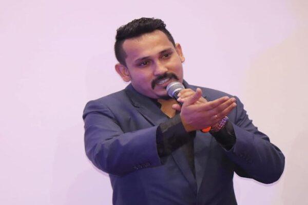 Man in a blue suit holding a microphone while speaking at an event or presentation.