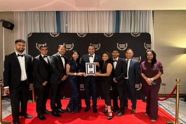 A group of nine individuals dressed in formal attire posing together at an award ceremony event.