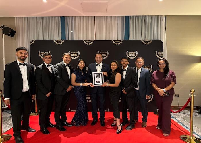 A group of nine individuals dressed in formal attire posing together at an award ceremony event.