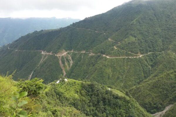 Winding road through a lush green mountainous landscape with steep slopes and vegetation.