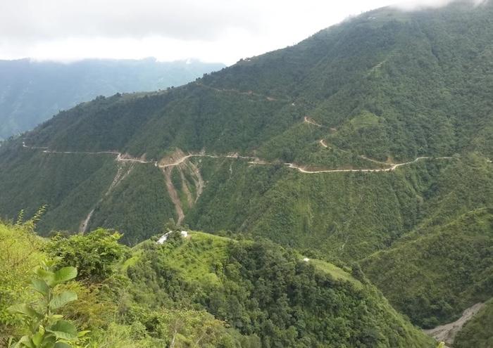Winding road through a lush green mountainous landscape with steep slopes and vegetation.
