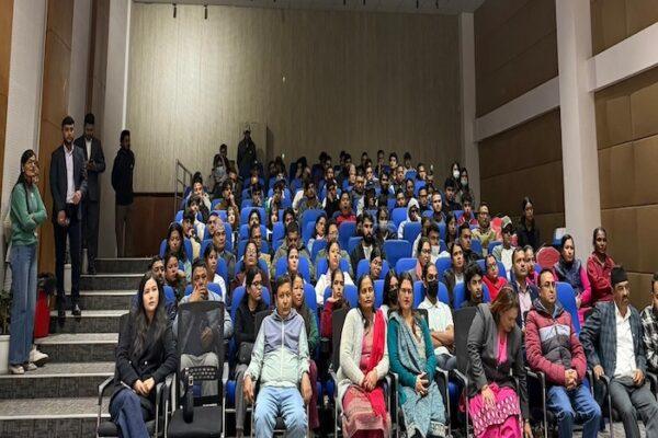 Large audience seated in a conference hall with blue chairs during an event.