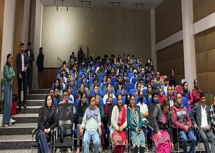Large audience seated in a conference hall with blue chairs during an event.