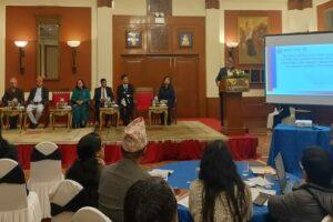 Panel discussion with speakers seated at a table in a conference setting, featuring a presentation screen.