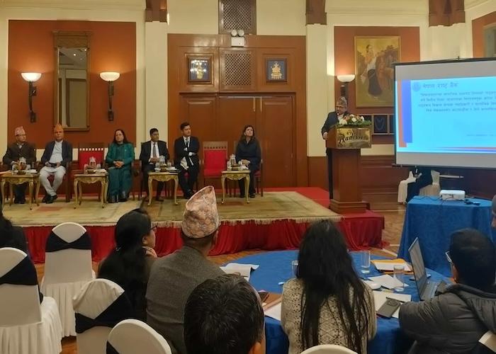 Panel discussion with speakers seated at a table in a conference setting, featuring a presentation screen.